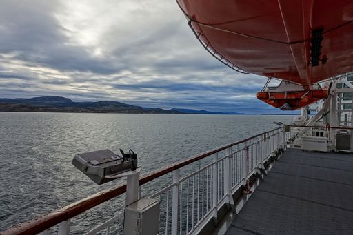 A beautiful Norwegian fjord landscape seen from a Hurtigruten ship on an overcast day with a red signal colored lifeboat on the right