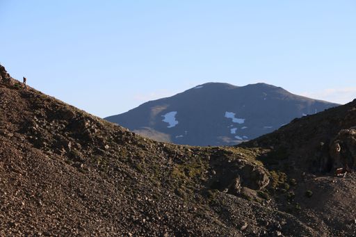 A lone hiker on a rocky mountain ridge with a distant snow-capped peak under a clear blue sky, showcasing the beauty of nature.