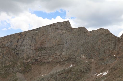 Rocky mountain landscape under a partly cloudy sky, showcasing rugged terrain and patches of snow, ideal for outdoor and nature themes.