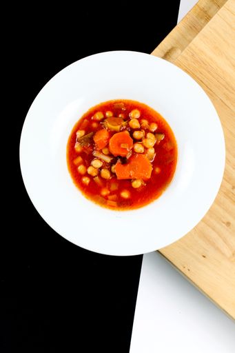 A top view of a chickpea soup with carrot in a white bowl on a wooden surface
