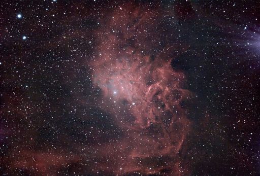 An image of a nebula in deep space, featuring intricate patterns of red gas and a field of stars.