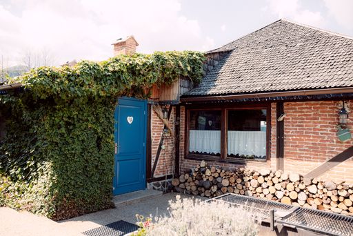 Charming rustic house with ivy-covered walls, a blue door, and stacked firewood, set under a bright sky.