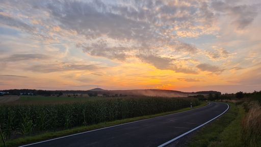 Oschatzer Hutberg at cloudy  sunset. With road and cornfield on the right.