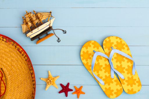 A cool view on painted light blue wood table with flip flops, sailboat, hat, and starfish