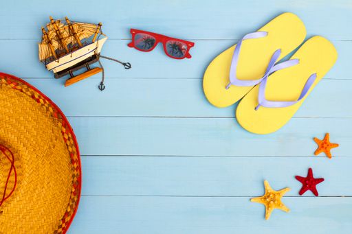 A cool view on painted light blue wood table with sunglasses, flip flops, sailboat, hat, and starfish