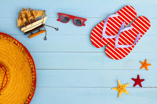 A cool view on painted light blue wood table with sunglasses, flip flops, sailboat, hat, and starfish