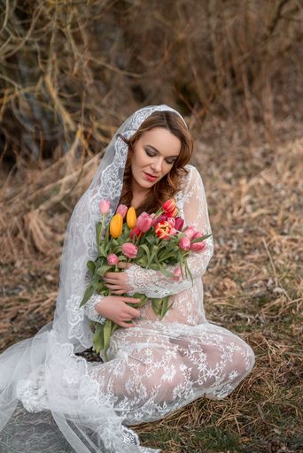 A shallow focus shot of a pregnant Caucasian woman wearing a white wedding dress and holding flowers