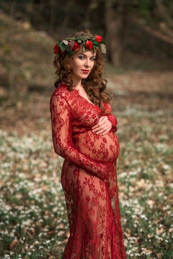 A shallow focus shot of a pregnant Caucasian woman wearing a red dress and a flower headband