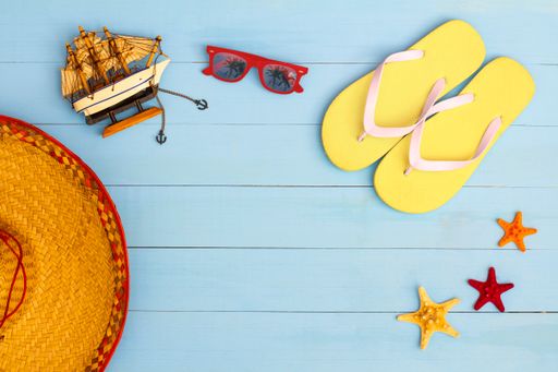 A cool view on painted light blue wood table with sunglasses, flip flops, sailboat, hat, and starfish