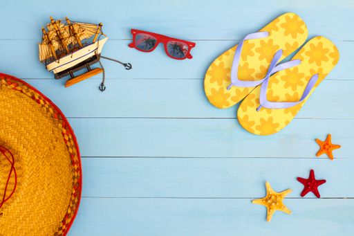 A cool view on painted light blue wood table with sunglasses, flip flops, sailboat, hat, and starfish