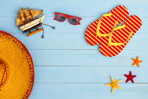 A cool view on painted light blue wood table with sunglasses, flip flops, sailboat, hat, and starfish
