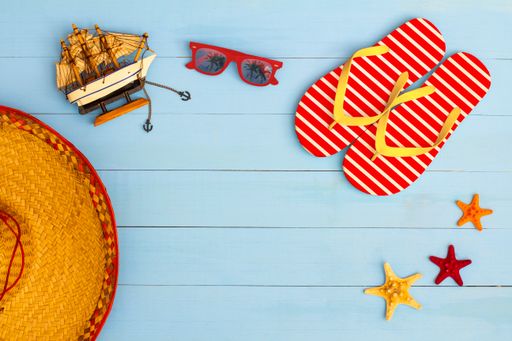 A cool view on painted light blue wood table with sunglasses, flip flops, sailboat, hat, and starfish