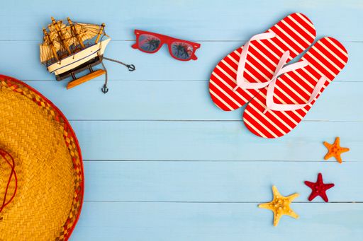 A cool view on painted light blue wood table with sunglasses, flip flops, sailboat, hat, and starfish