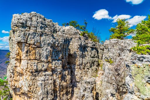 Majestic rock formations under a vibrant blue sky with scattered clouds, surrounded by green pine trees, showcasing natural beauty.