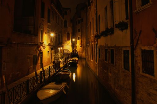 A serene night view of a Venetian canal with softly lit buildings and boats reflecting in the water.