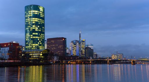 Skyline of Frankfurt at dusk with illuminated skyscrapers reflecting on the Main River.