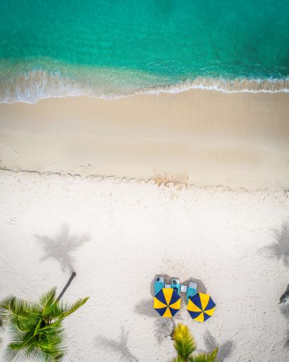 An aerial shot of folding chairs and umbrellas on the beach surrounded by the sea