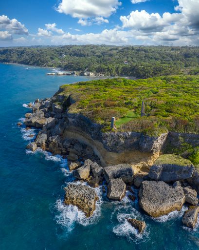 A vertical shot of cliffs covered in greenery surrounded by the sea under a blue cloudy sky