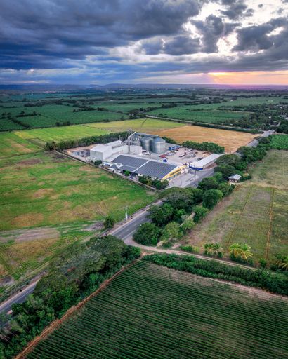 A vertical shot of a factory and a warehouse with solar panels in a field under a stormy sky