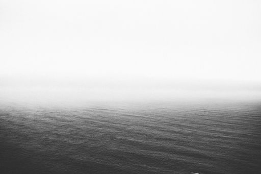 A greyscale shot of the calm ocean slowly disappearing at the horizon - perfect for background