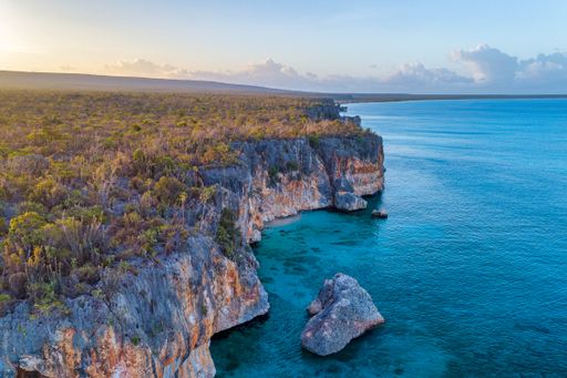 A landscape of rocky cliffs covered in greenery surrounded by the sea during the sunrise