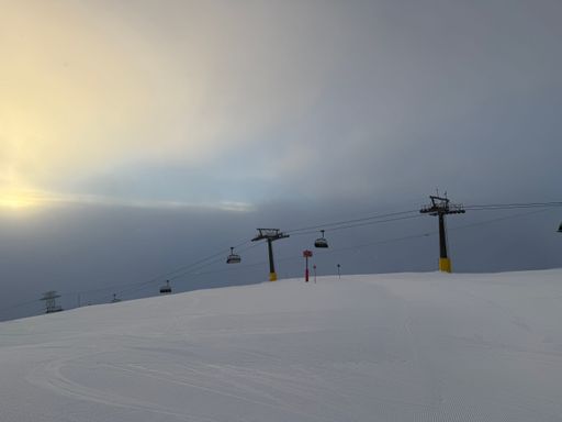 Ski lift under a cloudy sky on a snowy mountain slope at sunrise, capturing the serene winter landscape.