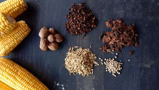 A top view of raw sweet corns with peppers, nutmeg, and cloves on a wooden table