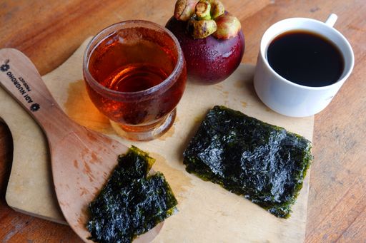 A close up of chopped seaweed and a cup of coffee and Mangosteen beside it on a wooden table