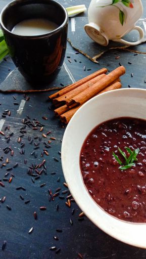A vertical shot of cinnamons, a glass of milk, and a bowl of red meal on a black table