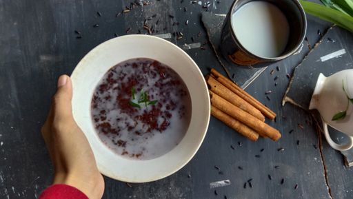A top view of black glutinous rice porridge and coconut milk with cinnamon sticks