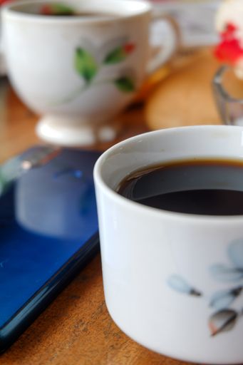 A vertical, close-up shot of a cup of coffee and a blue smartphone on a table