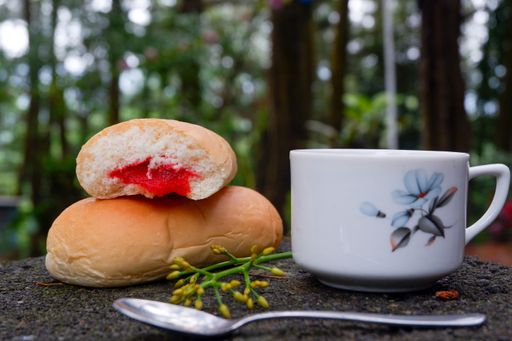 A close up of bread with strawberry jam with a cup of tea with blurred forest in background