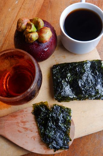 A vertical shot of a cup of coffee and mangosteen with tea on a wooden surface