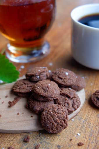 A selective focus shot of chocolate cookies on a background of a cup of coffee and tea