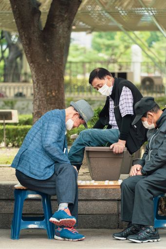A group of South Korean seniors wearing face masks sitting outside and playing a leisure game