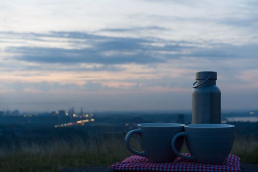 A closeup shot of two cups and a can in the landscape with city lights and cloudy sky in background