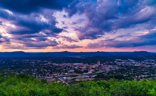 A stunning aerial view of Roanoke, Virginia at sunset with vibrant clouds and cityscape below.