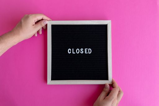 A man's hands holding a small black board with CLOSED writing against a pink background