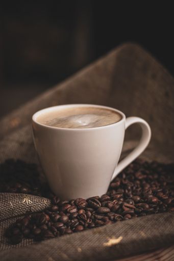 A vertical shot of a cup of coffee and beans on a piece of fabric