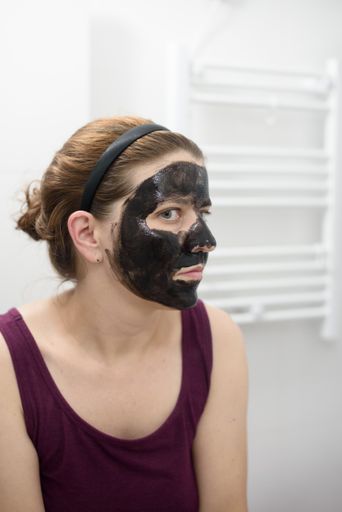 A vertical shot of a Spanish Caucasian woman with a charcoal face mask on her, in her bathroom