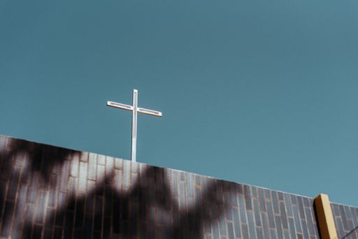 a low angle shot of a metallic cross on a structure under blue sky