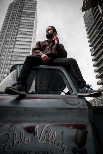 A low-angle shot of a cool sexy young Hispanic man sitting on the truck roof and smoking