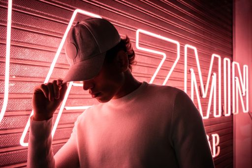 A portrait of a young Hispanic man with a cap posing near pink neon lights