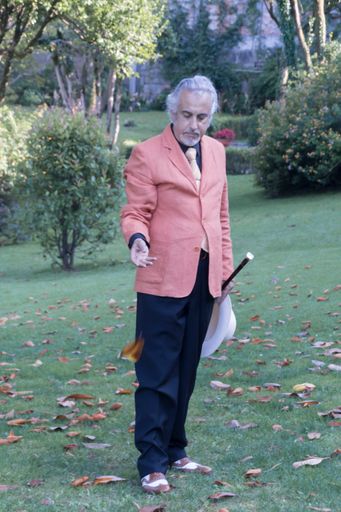A man in a light orange suit standing in the park with the trees in the background