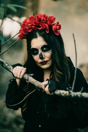 A vertical shot of a woman with Halloween makeup and a flower crown, in a spooky forest