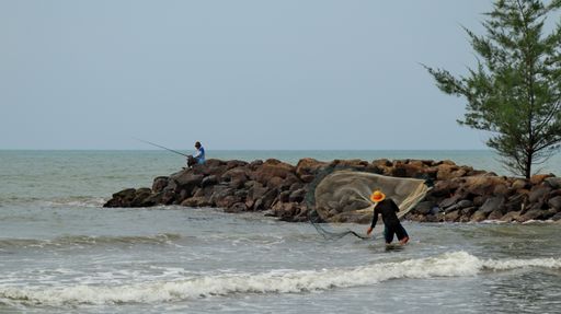 Two fishermen on a rocky shore on a gloomy day