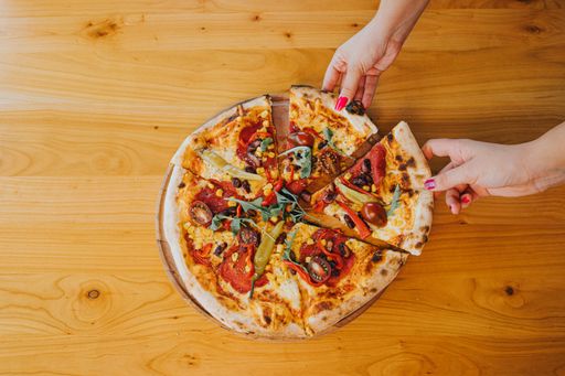 An overhead shot of two female hands taking slices from the whole pizza