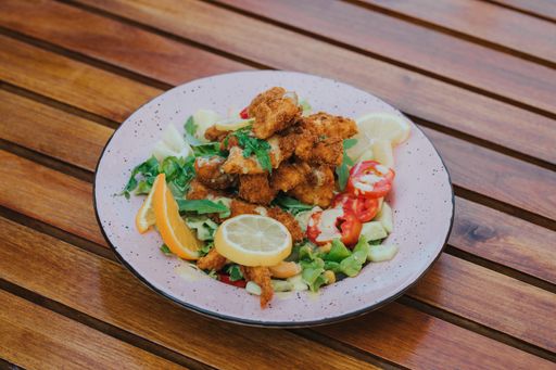 A high angle shot of a salad with nuggets on a white plate on wooden table