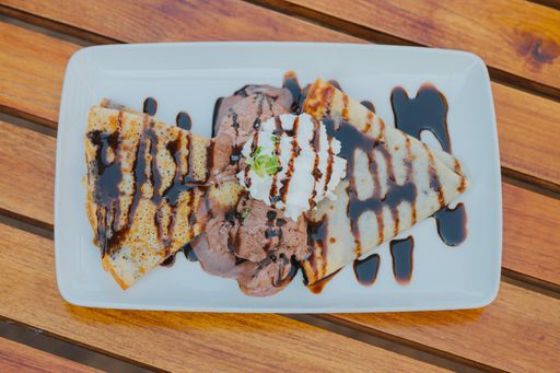 A top view of crepes with whipped cream and chocolate sauce on a plate on the table
