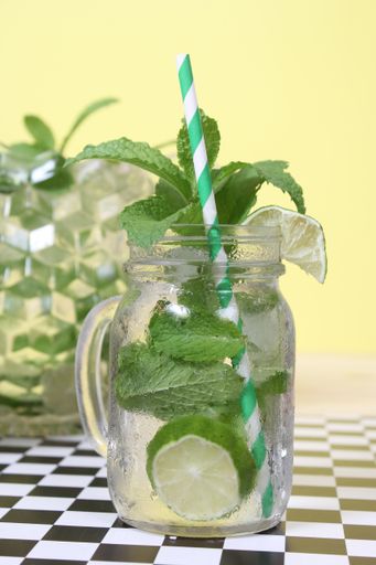 A selective focus shot of a mojito cocktail in a glass with a straw on a checkered surface